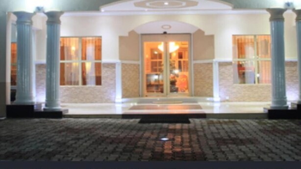 L’entrée d’un hôtel, avec une porte centrale encadrée de colonnes, et un dallage menant à cette porte.