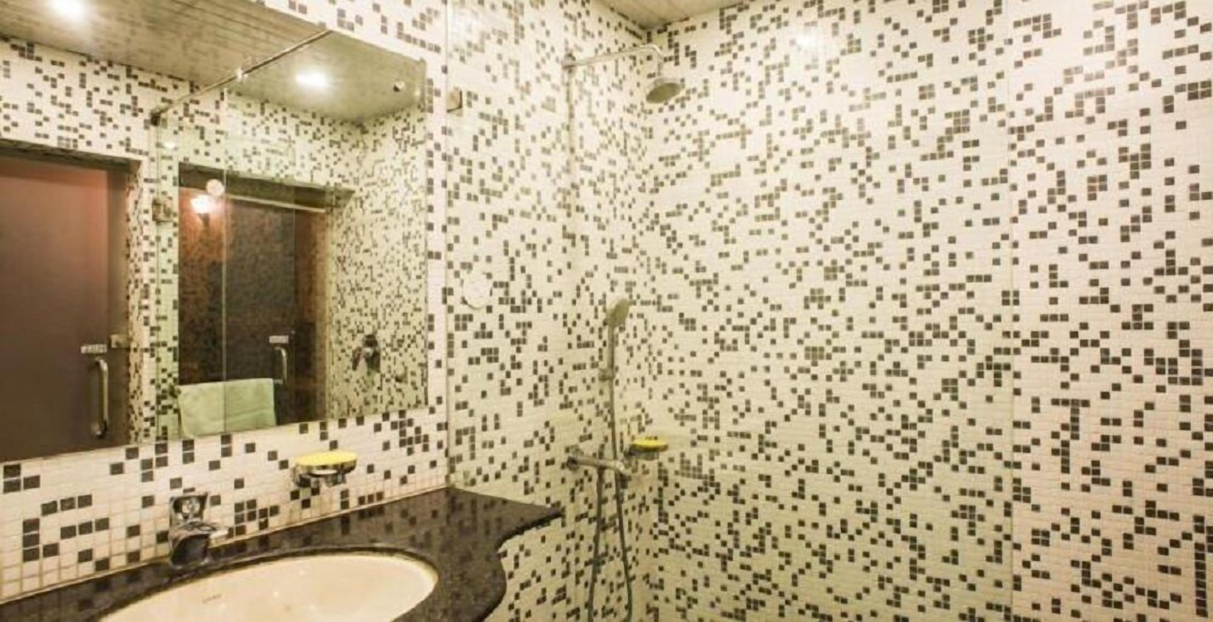 A bathroom with a mosaic tile wall, a sink, and a shower.