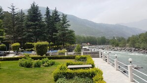 Une promenade au bord de la rivière, offrant une vue sur le cours d’eau, entourée de verdure et de montagnes.