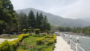 Une promenade au bord de la rivière, agrémentée d’une rambarde, entourée d’une végétation luxuriante et avec une chaîne de montagnes en toile de fond.