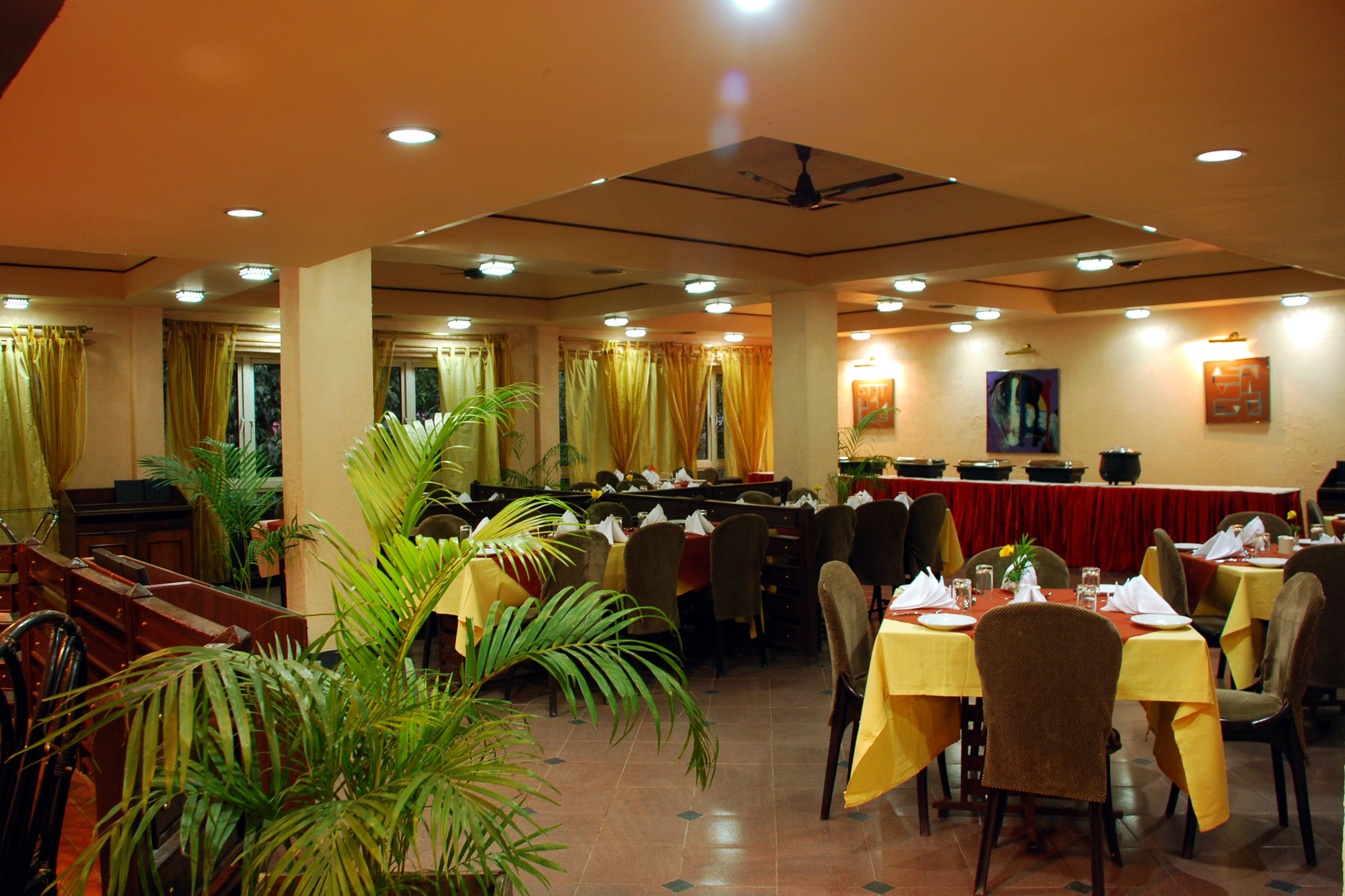 Un restaurante con varias mesas y sillas, un ventilador de techo y plantas en macetas.