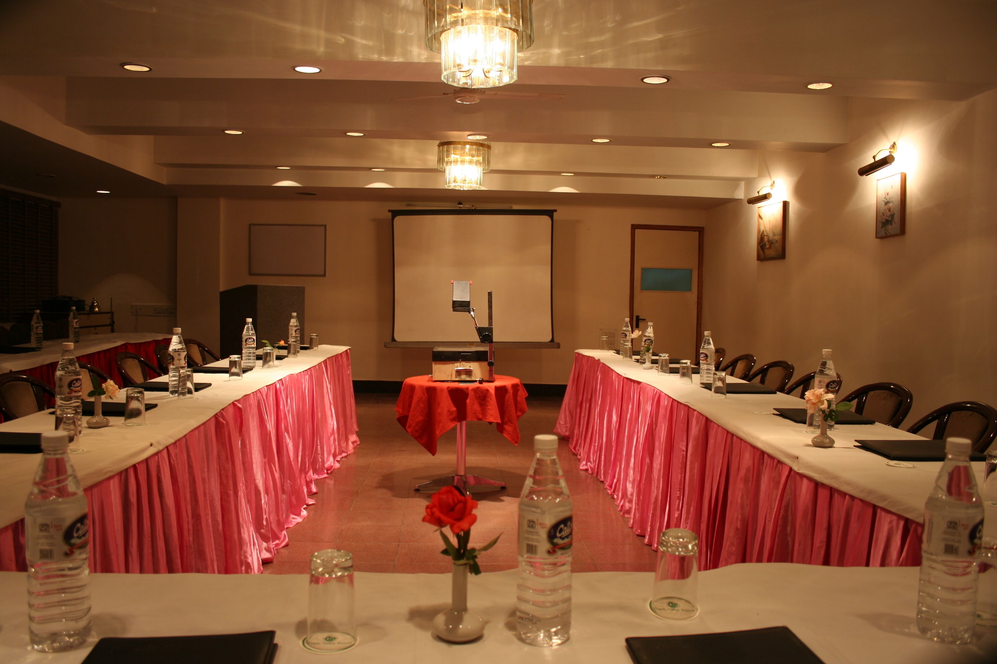 A conference room with tables set for a meeting, equipped with water bottles, a projector, and a screen.