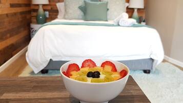 A hotel room with a bed, a bedside table with a bowl of fruit, and a wooden wall.