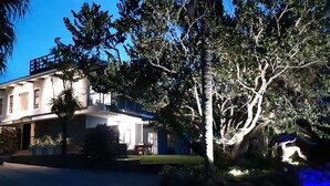 Een goed verlicht woonhuis met een ruime woning, oprit en een aangelegde tuin met een palmboom.