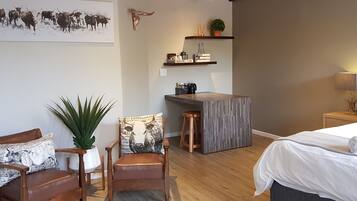 Um quarto aconchegante com uma cama, uma cadeira de madeira, uma mesa pequena e uma prateleira na parede com objetos decorativos.