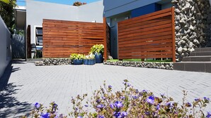 Een modern gebouw met een stenen muur en houten lamellen, een geplaveid binnenterrein en potplanten.