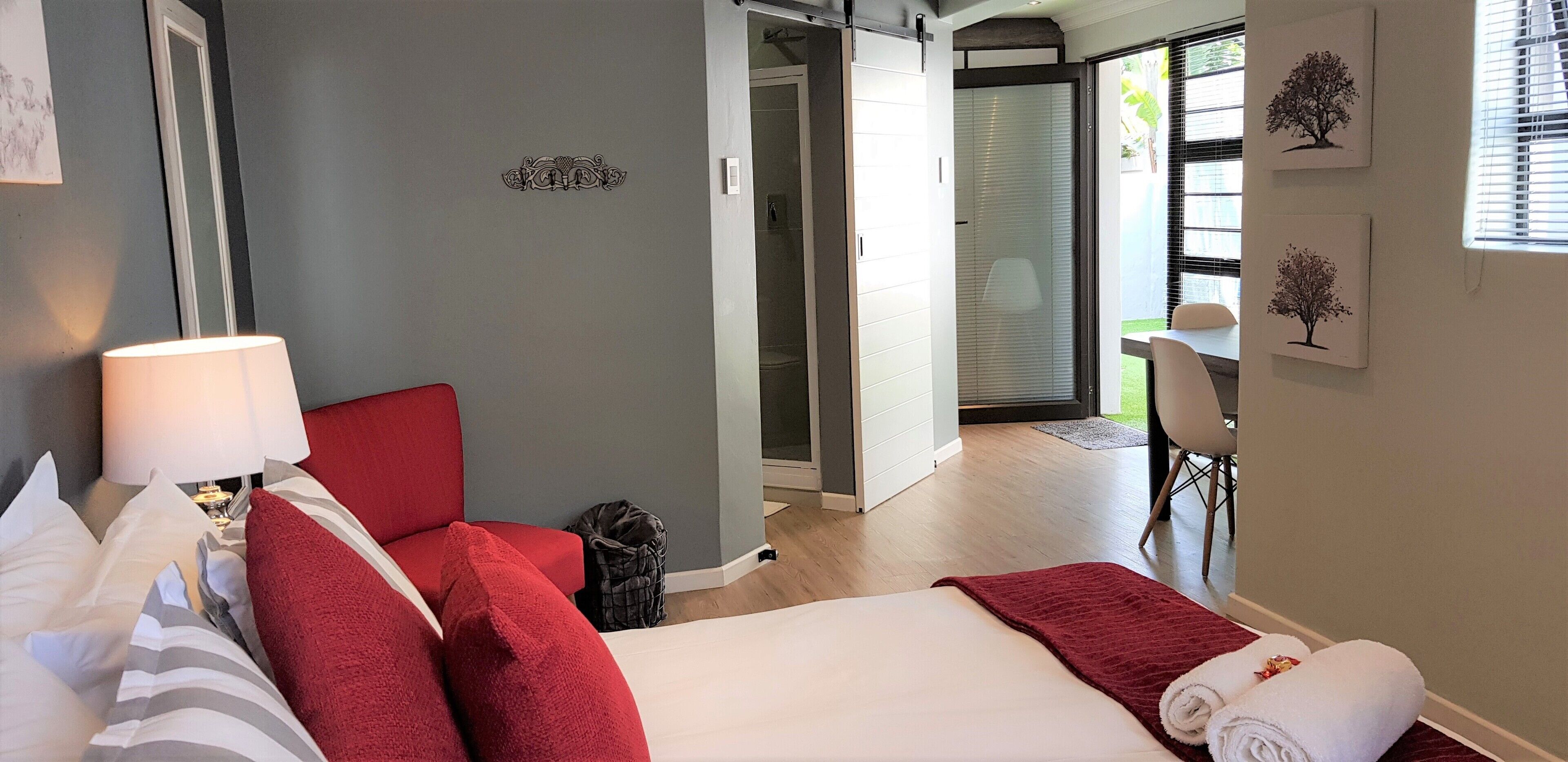 Una habitación de hotel con una cama, una silla roja, un escritorio y una ventana con persianas.