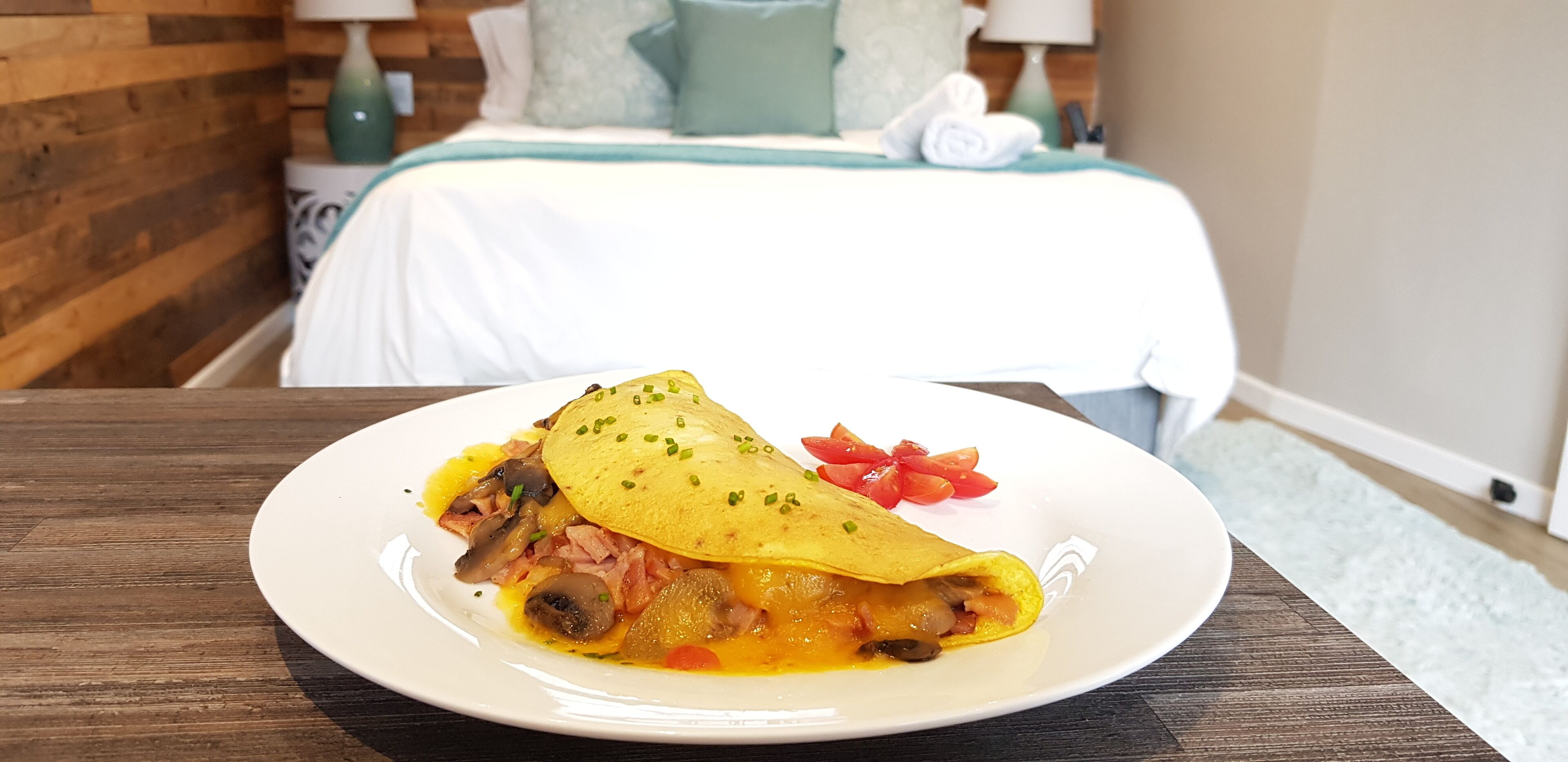Ein Teller Essen auf einem Holztisch, im Hintergrund ein Bett und ein Nachttisch.