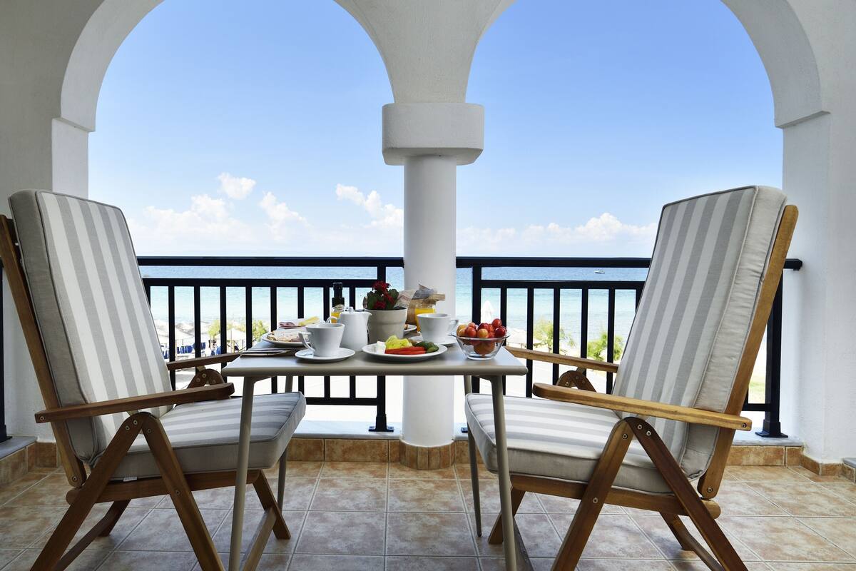 A balcony with two chairs and a table, overlooking a clear blue sea.