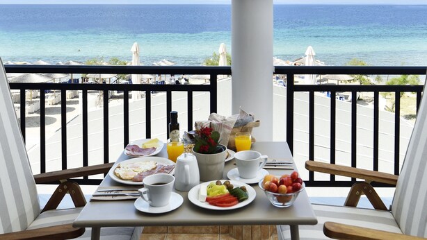 A balcony table with breakfast items, a view of the ocean, and beach umbrellas. - Assano Sea Front Luxury (Sithonia)