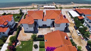 An aerial view of a coastal residential area with houses featuring red-tiled roofs, a beach in the background, and a clear view of the ocean. - Assano Sea Front Luxury (Sithonia)