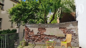 A courtyard with a brick wall, a wicker chair, and a small table with a green mat. - Apartment im Luisenviertel - Grün (Wuppertal)