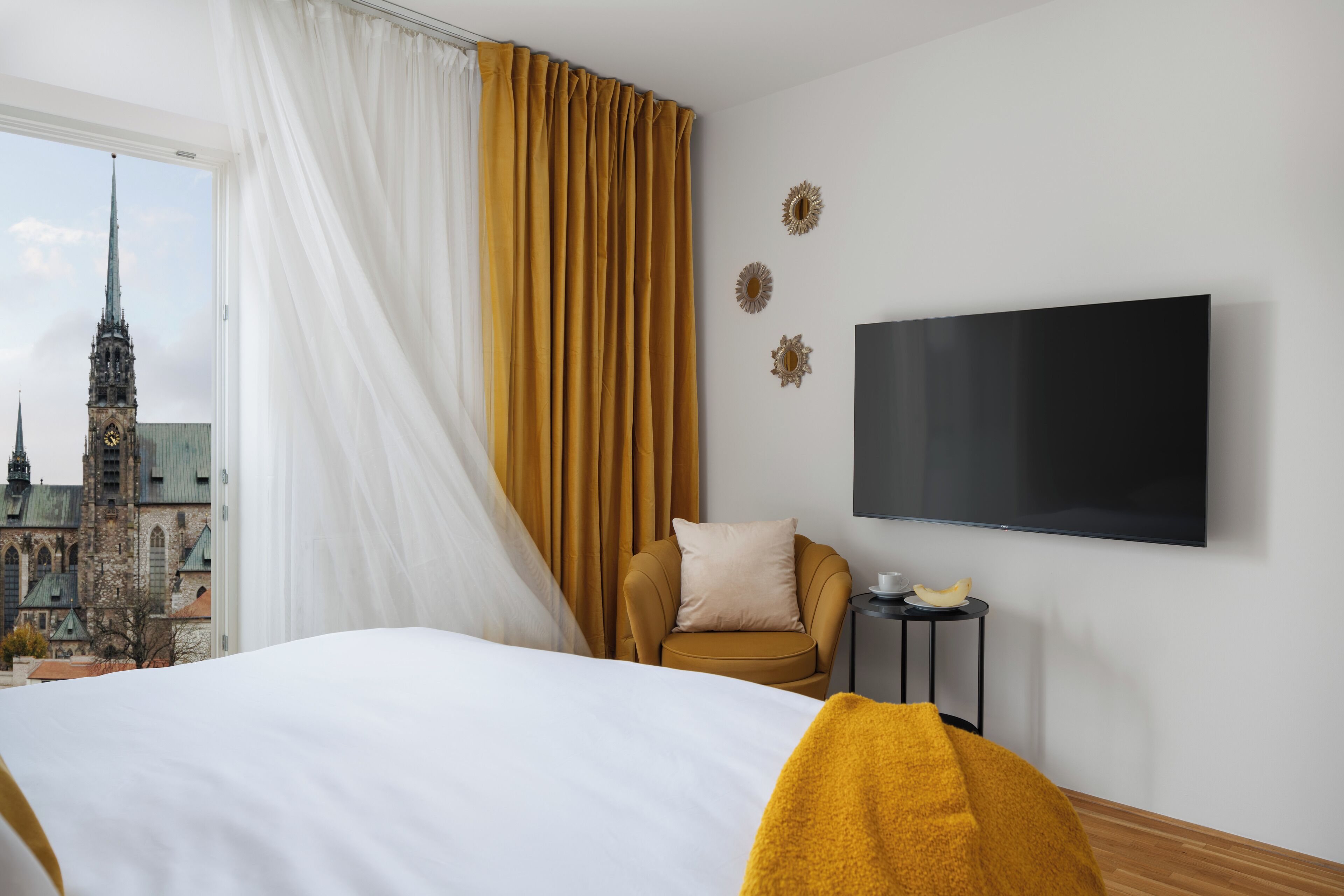 Une chambre d’hôtel avec un lit, une chaise, une télévision et une vue sur un bâtiment historique.