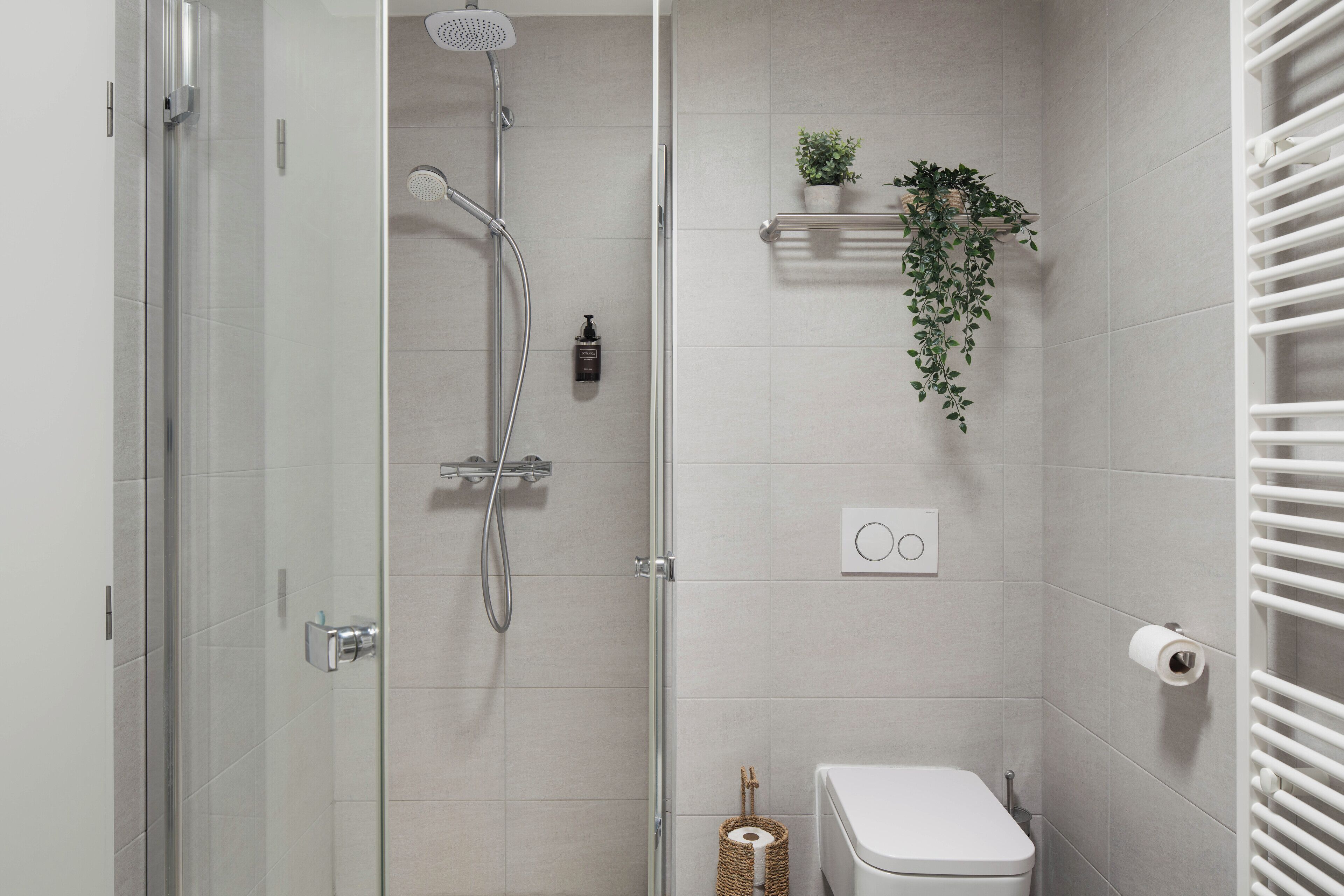A modern bathroom with a glass shower enclosure, a toilet, a towel rack, and a small shelf with a plant.