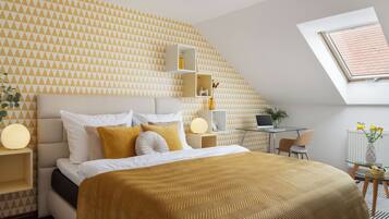 A modern bedroom with a geometric patterned wall, a bed with a gold throw, a desk with a laptop, and a skylight.