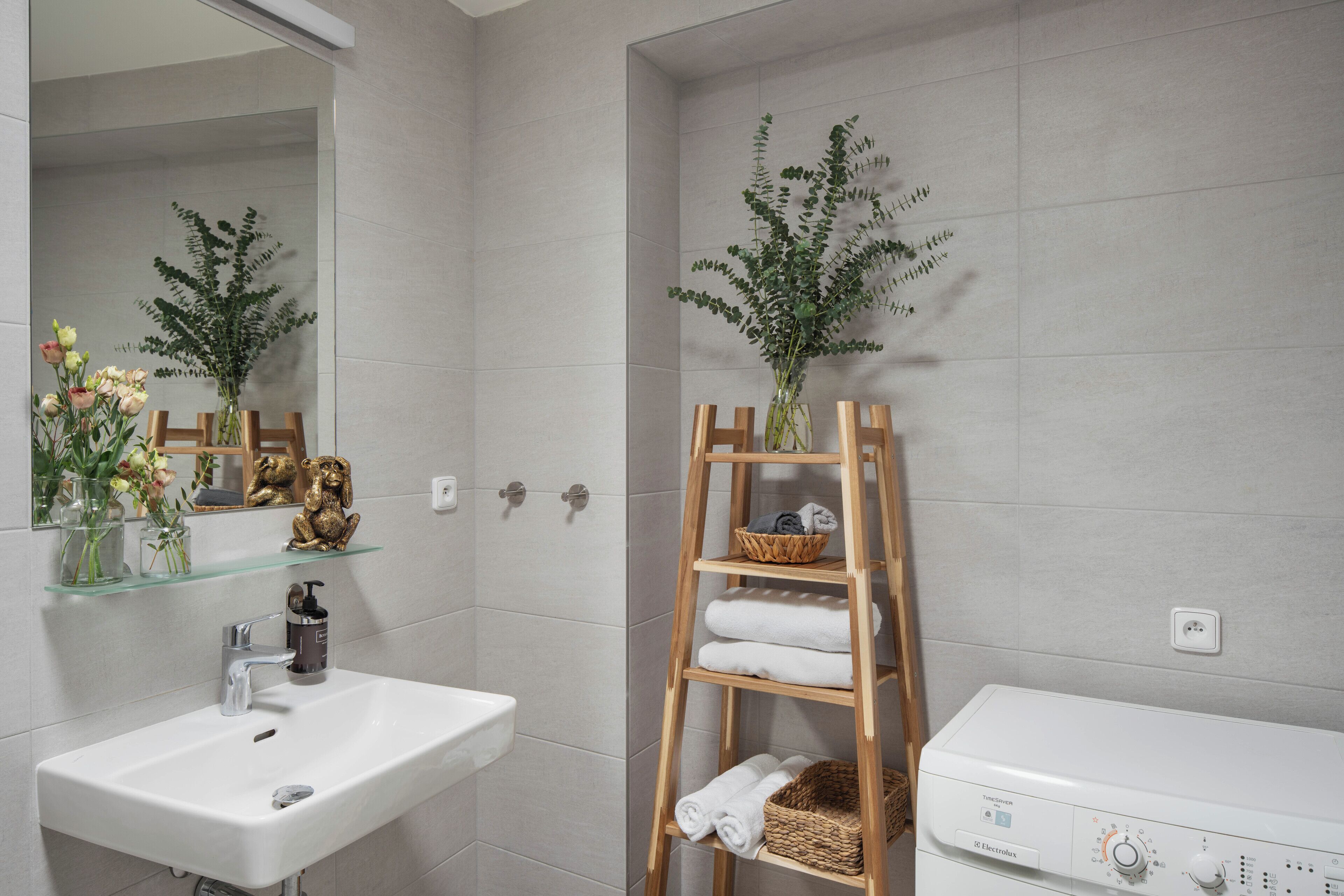 Une salle de bain avec un lavabo blanc, une étagère en bois où sont posées des serviettes et un radiateur électrique blanc.