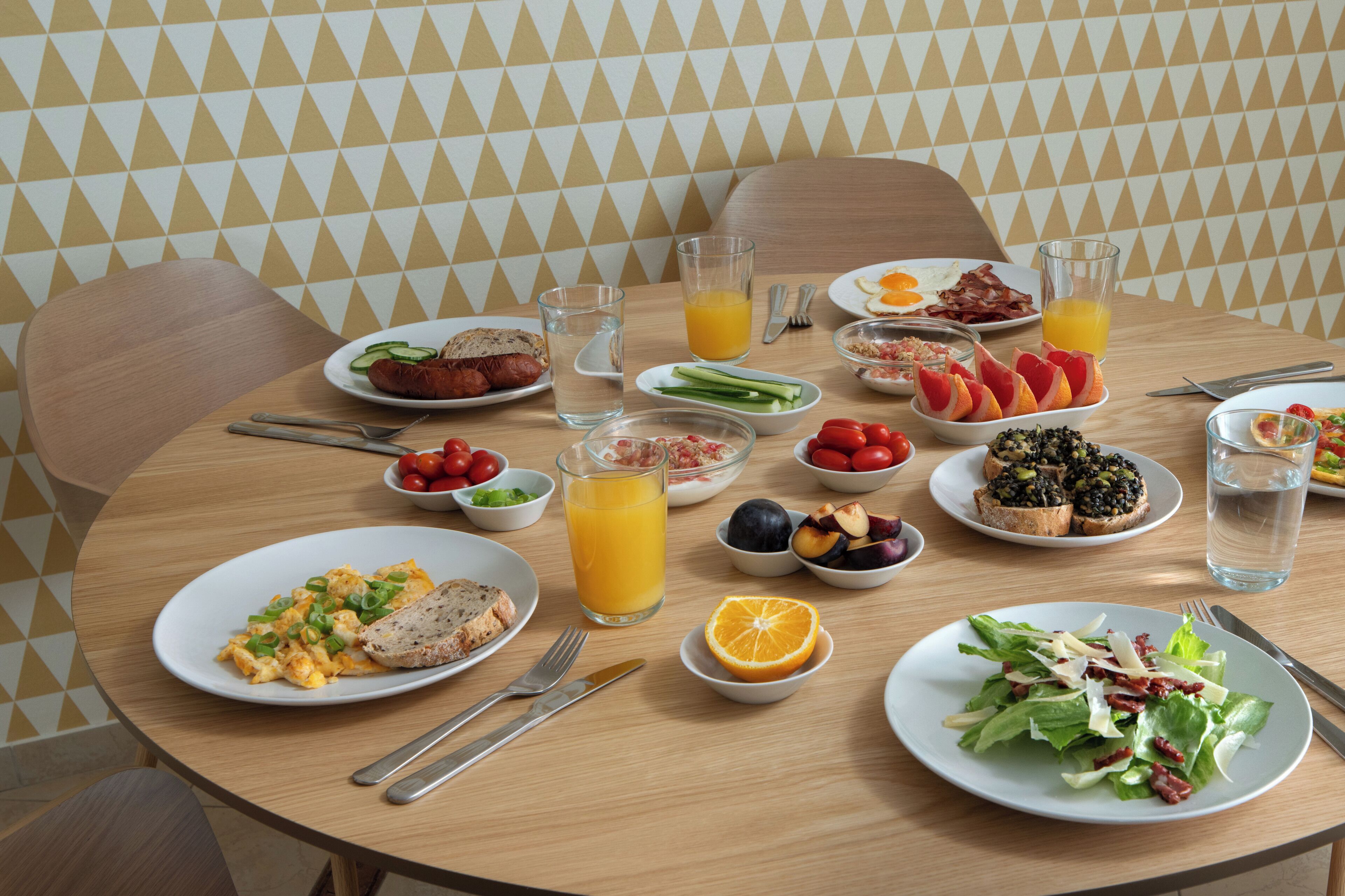 A breakfast table with various dishes, including eggs, bacon, toast, and a salad.