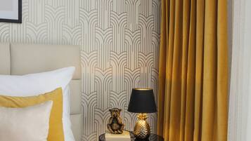 A neatly made bed with white and mustard pillows, a small round table with a lamp, and a gold decorative item.
