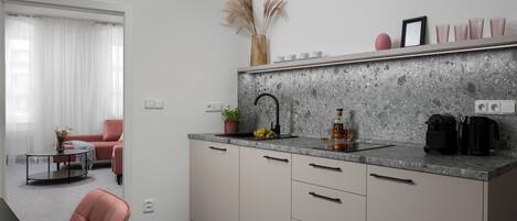 A modern kitchen with a granite countertop, a sink, and a coffee machine. There is a dining area with a table and chairs visible through an open door.