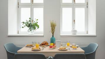 A dining table with plates of food, glasses of juice, and a vase with dried plants.