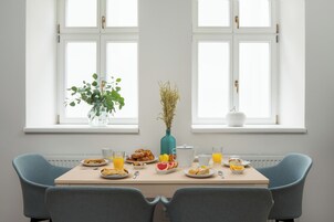 A dining table with plates of food, glasses of juice, and a vase with dried plants.