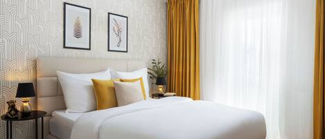 A neatly arranged bedroom with a large bed, a bedside table with a lamp, and framed botanical prints on the wall.