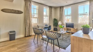 Een moderne woonkamer met houten vloer, een eethoek met glazen tafel en stoelen, een televisie en een grote potplant.