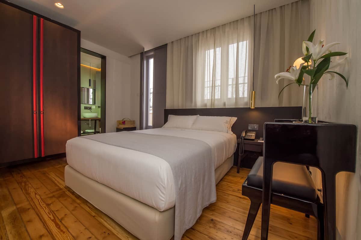 A hotel room with a large bed, a desk with a chair, a nightstand, and a vase with flowers.