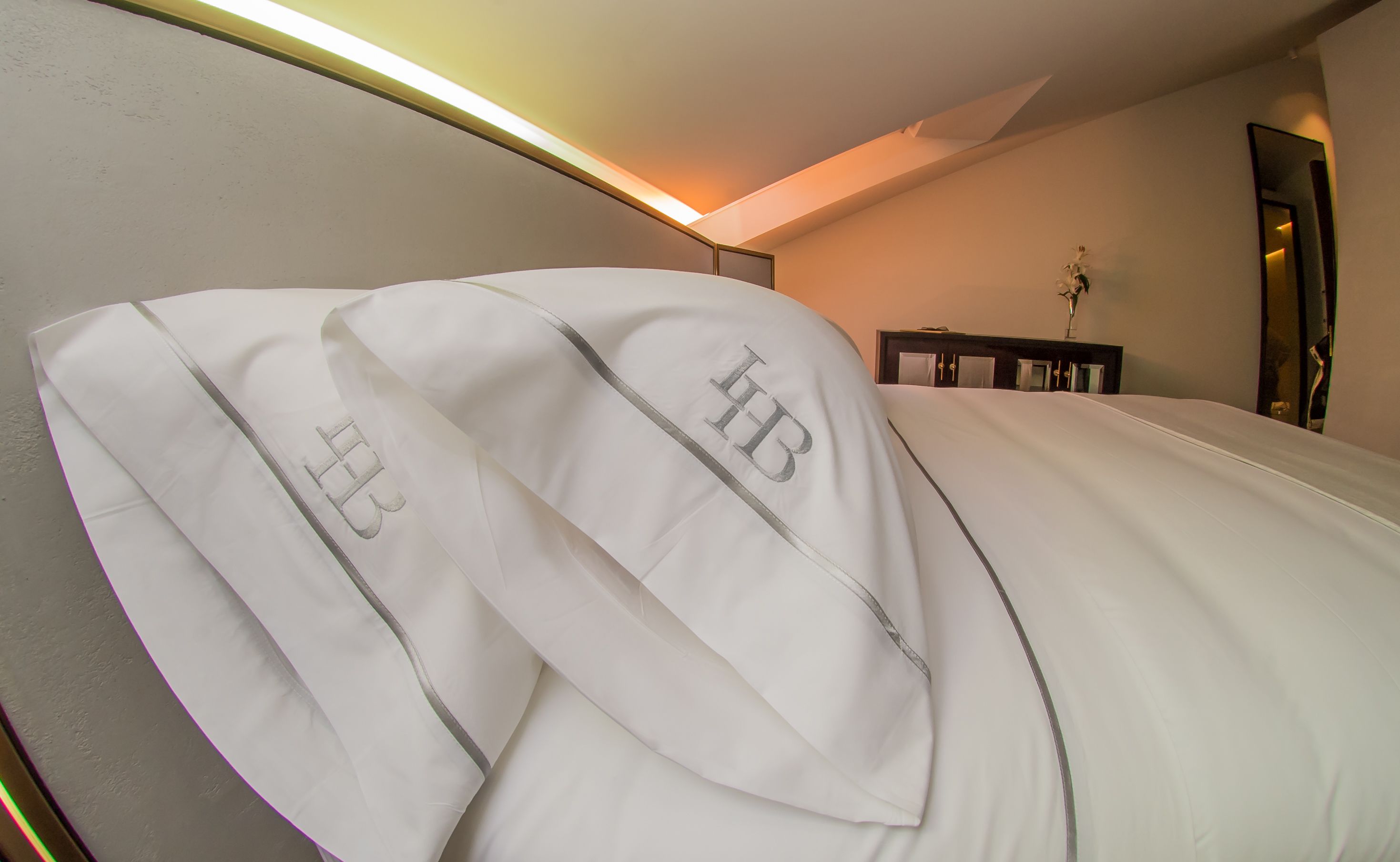 Ein Hotelzimmer mit einem aufgeräumten Bett, einem Nachttisch mit einer Vase und einem Spiegel an der Wand.