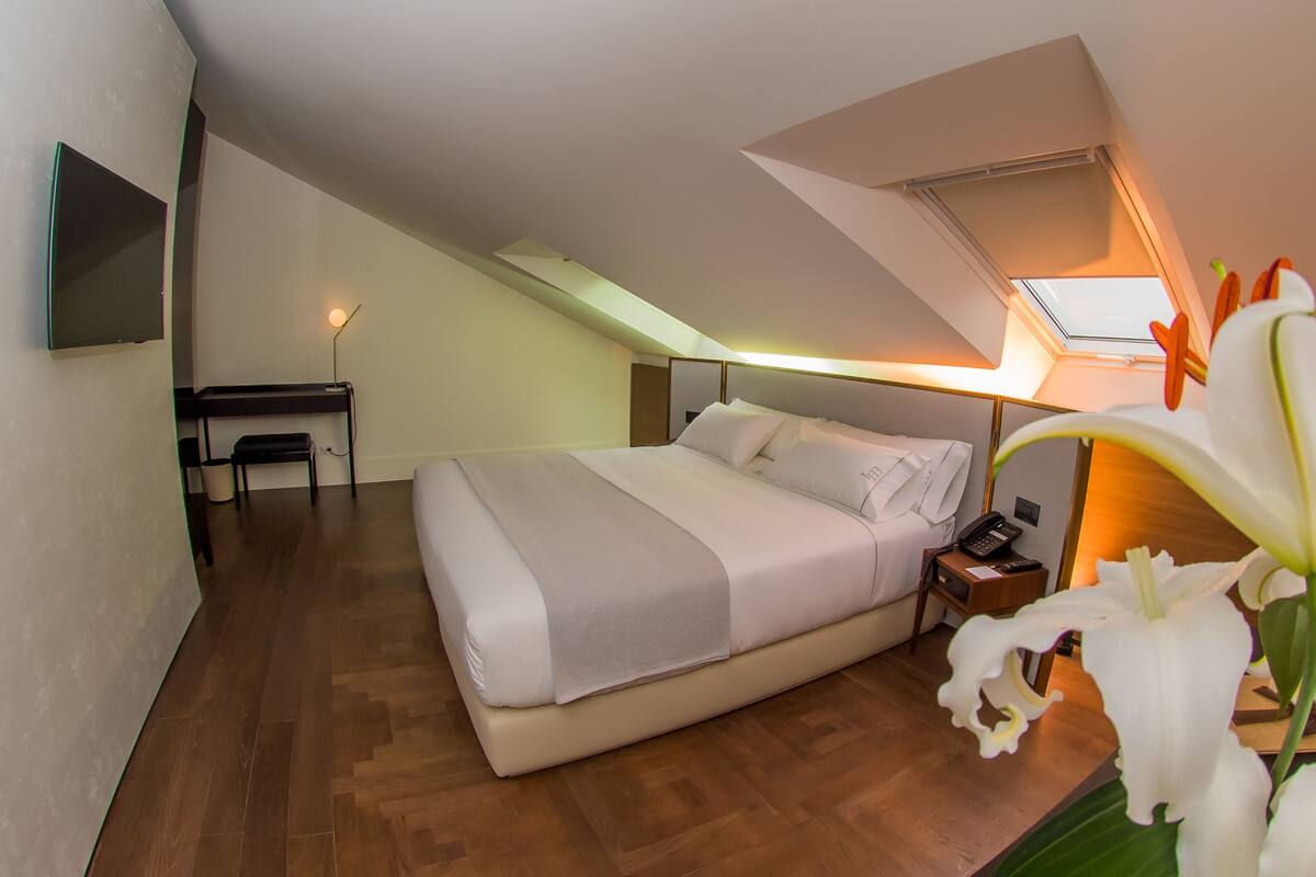 A bedroom with a bed, bedside table, lamp, and a desk with a chair.