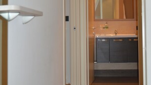 Un couloir étroit mène à une salle de bain équipée d’un lavabo et d’un miroir.