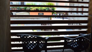 Un balcon donnant sur une rue et des immeubles, avec deux chaises noires et une table en métal.