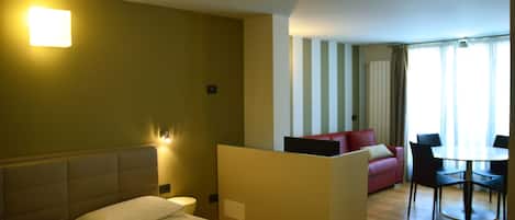 Habitación de hotel con cama, una mesita, un sofá y un área de comedor separada.