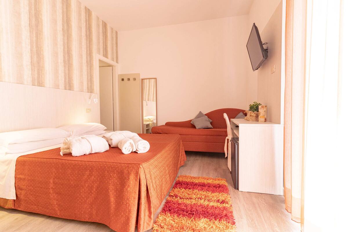 A hotel room with two beds, a desk, a mirror, and a TV.