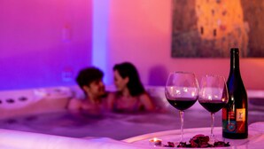 A hot tub with two glasses of red wine and a bottle, surrounded by rose petals. - Hotel Dusseldorf (Rimini)