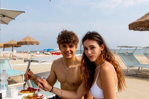A beachside dining table with a meal, beach umbrellas, and lounge chairs in the background. - Hotel Dusseldorf (Rimini)