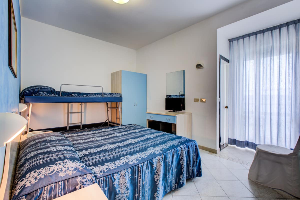A bedroom with a bunk bed, a desk with a TV, a chair, and a large window with curtains.