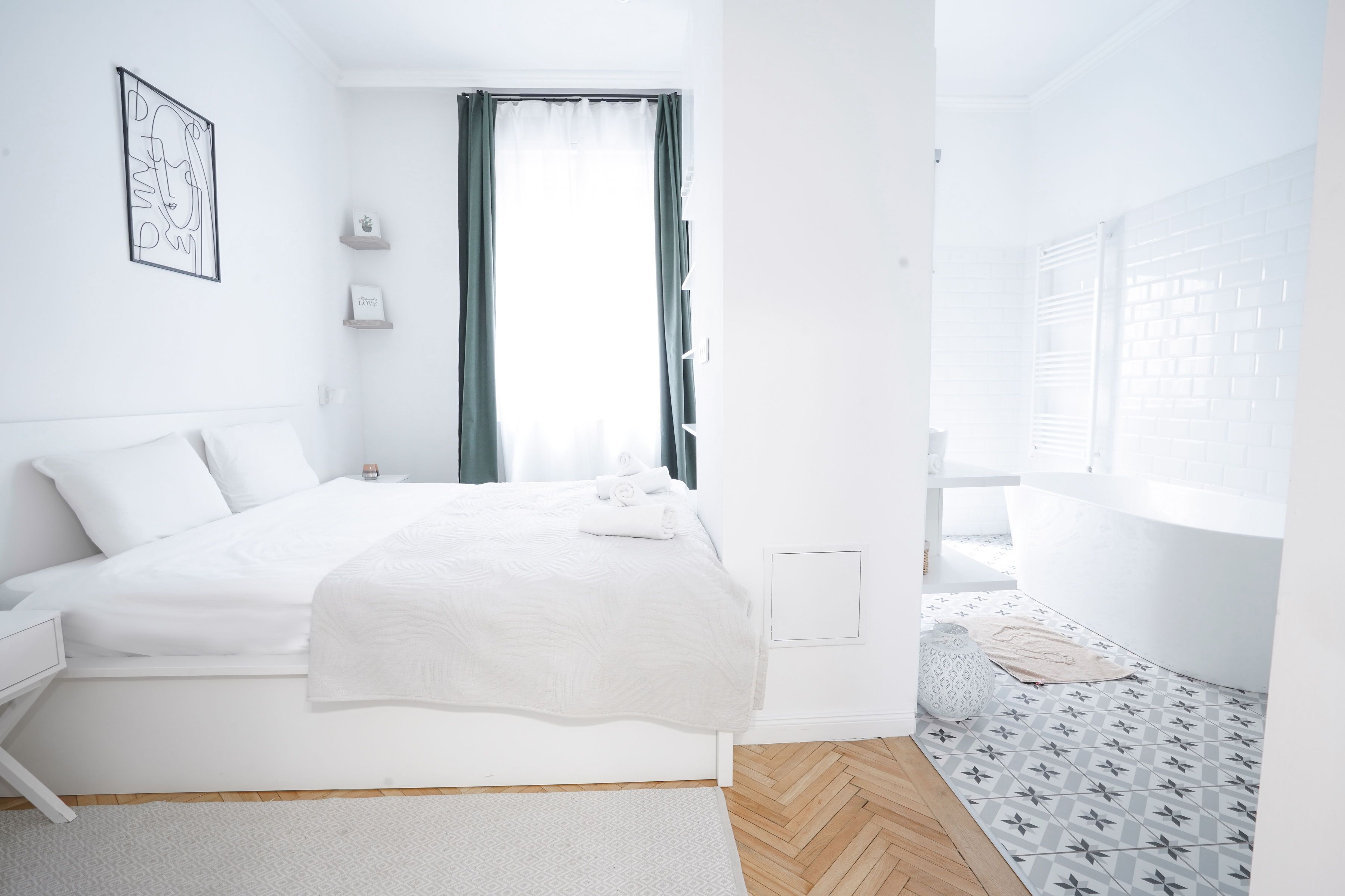 A modern bedroom with a neatly made bed, a bedside table, a window with curtains, and a patterned floor.