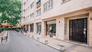 Vista de la calle con un edificio que tiene varias tiendas, aceras y pilares de seguridad.
