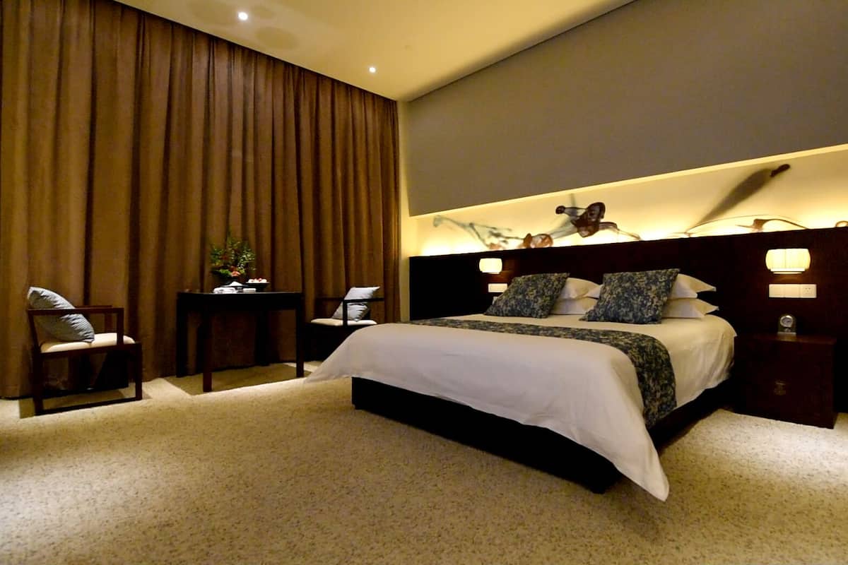 Una habitación de hotel moderna con una cama grande, un escritorio, una silla y una mesita de noche.
