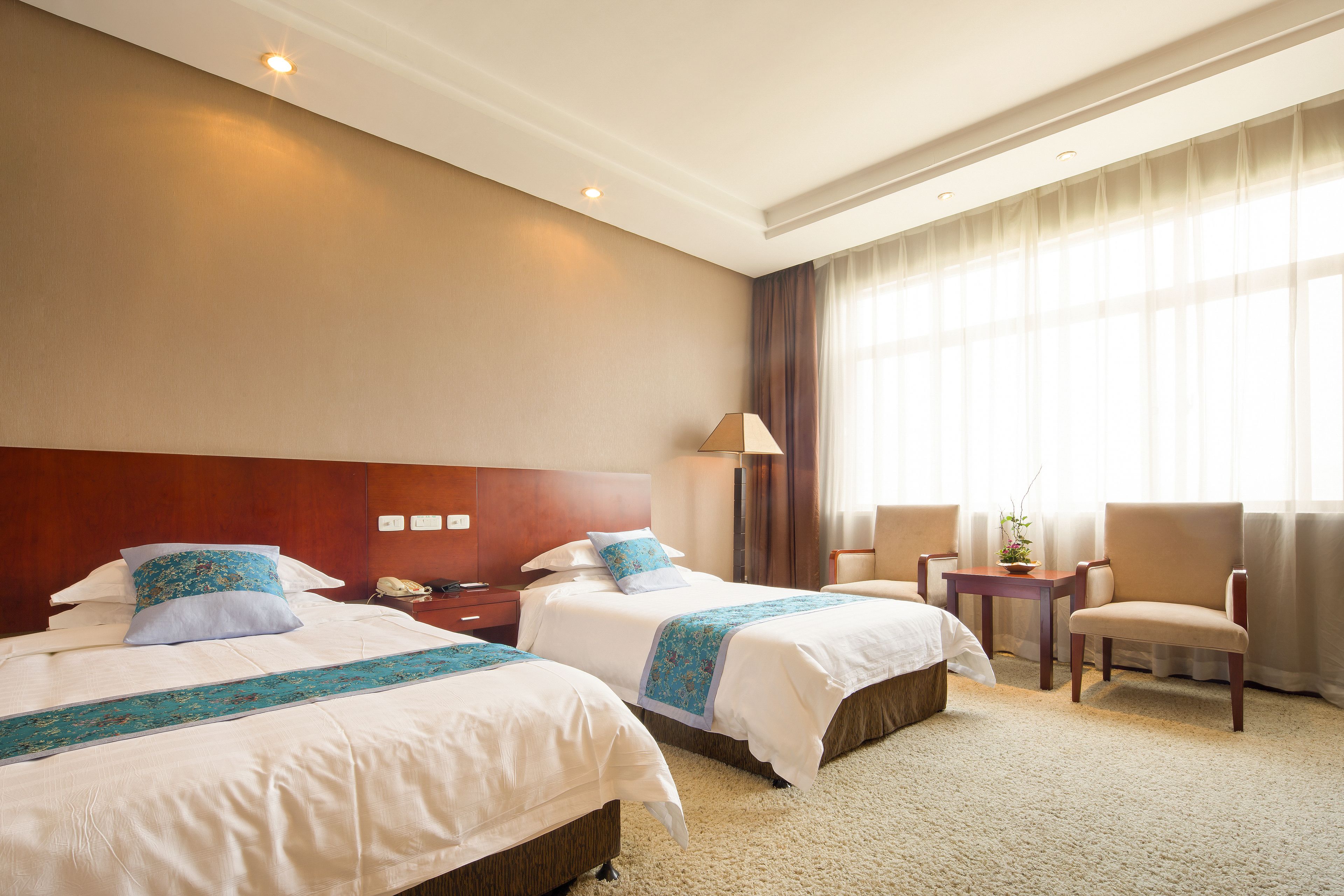 A hotel room with two beds, a nightstand, a lamp, a chair, and a window with curtains.