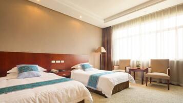 A hotel room with two beds, a nightstand, a lamp, a chair, and a window with curtains.