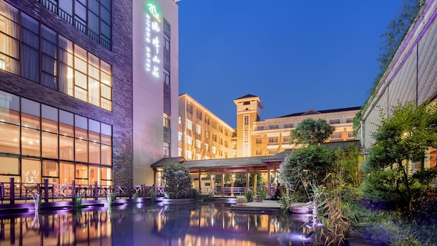 A hotel with a reflective pool, a covered outdoor seating area, and a prominent building with illuminated signage. - Jiuhua Mountain Xifeng Hotel (Chizhou)