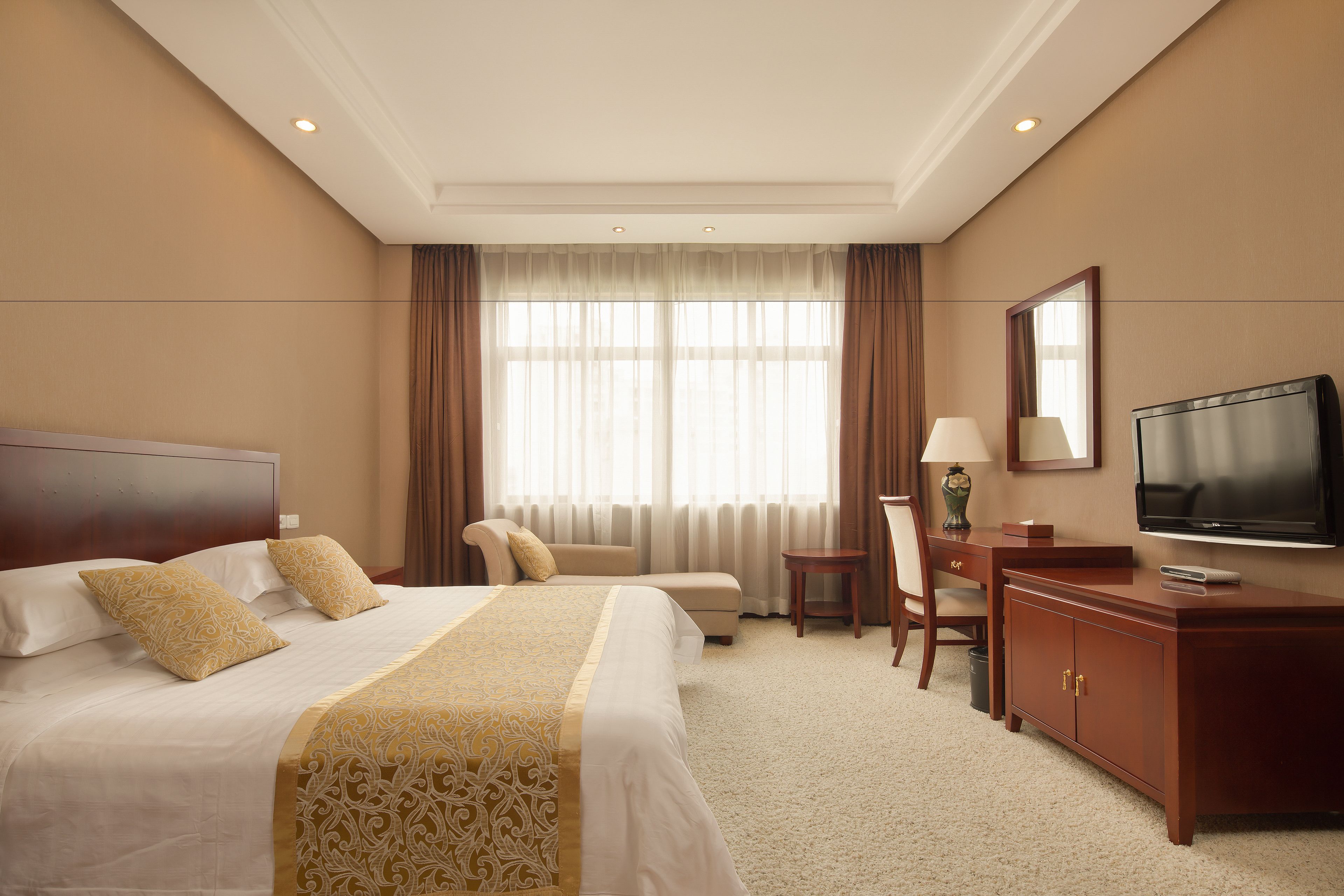 A hotel room with a large bed, a desk, a chair, a television, and a window with curtains.
