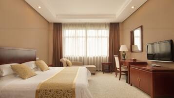 A hotel room with a large bed, a desk, a chair, a television, and a window with curtains.