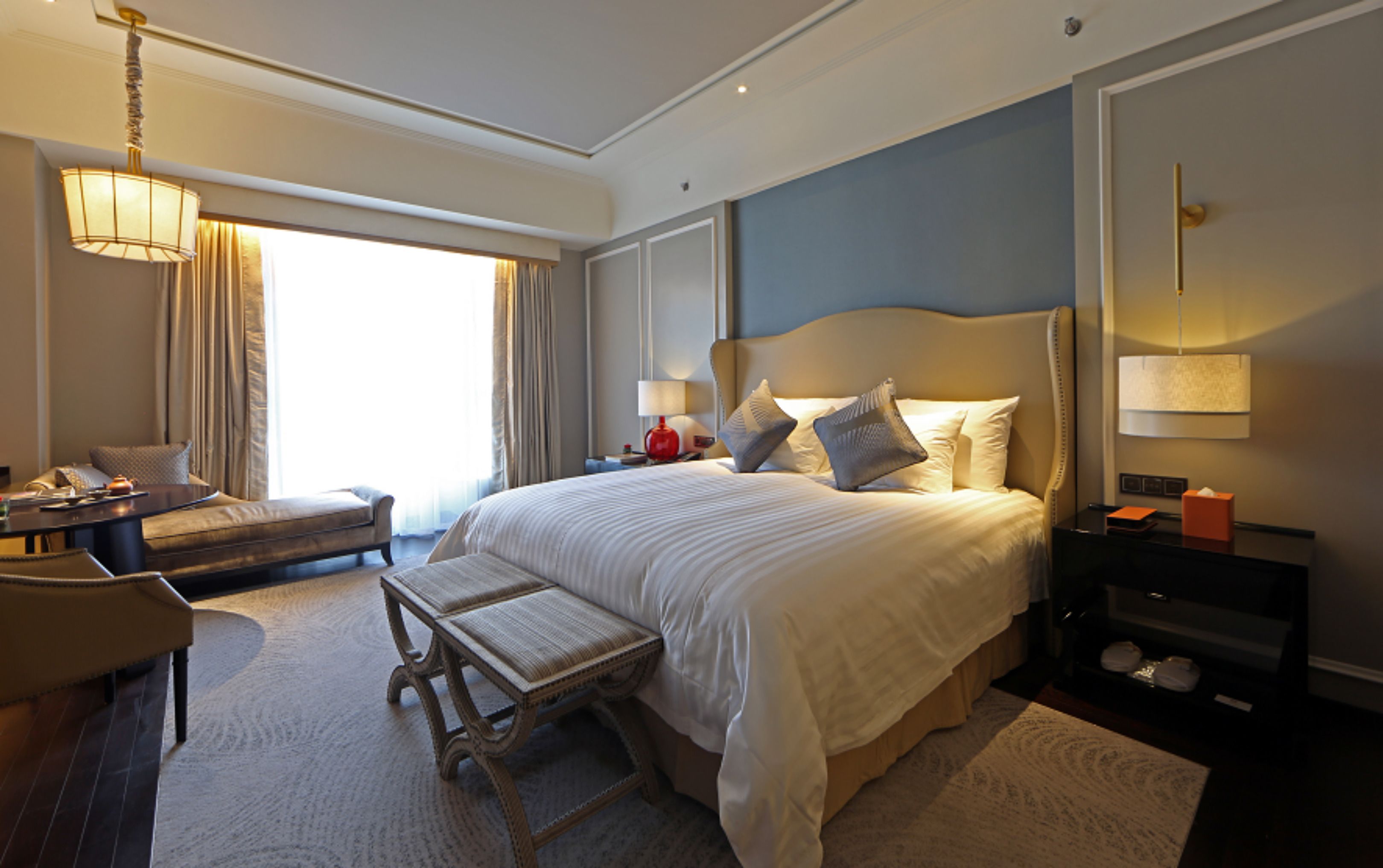 A hotel room with a large bed, a desk, a chair, and a window with curtains.