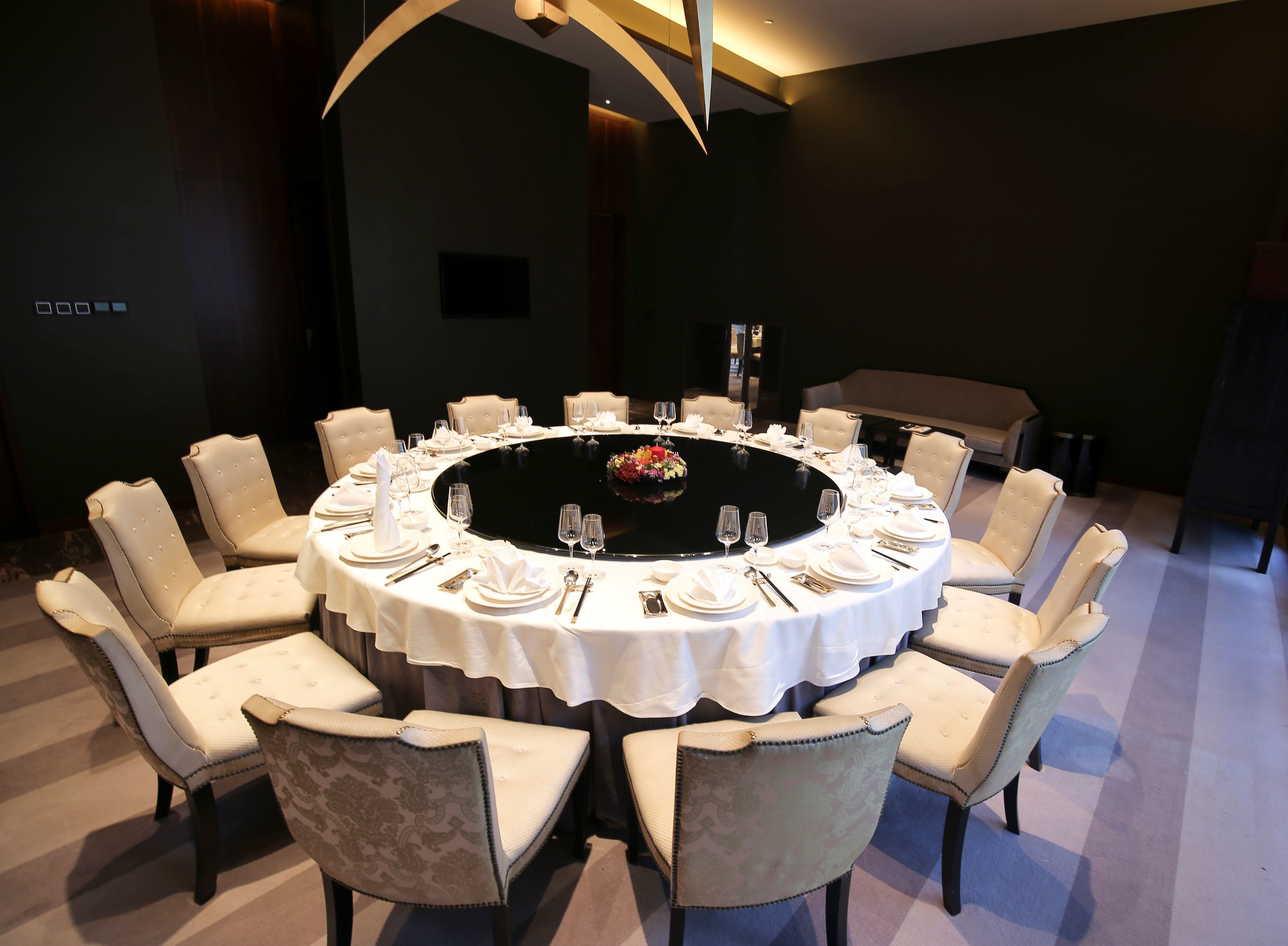 A round dining table with white tablecloth, surrounded by upholstered chairs with button-tufted backs.