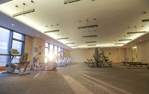 Een ruime fitnessruimte met diverse fitnessapparaten, grote ramen en een hoog plafond met inbouwverlichting.