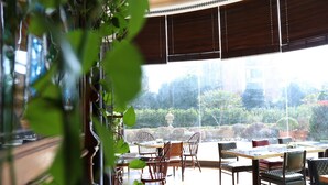 A dining area with a table and chairs, large windows, and a view of greenery outside. - Grand New Century Hotel Yixing (Wuxi)