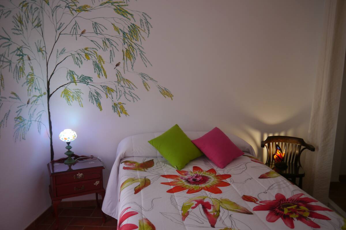 A bedroom with a bed, a nightstand, a lamp, and a chair.
